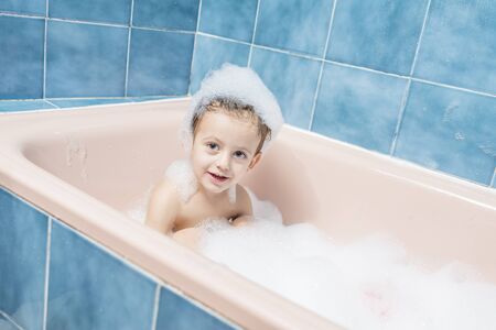 Color photography of a smiling child playing in the bath with his head full of foam.の写真素材