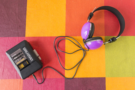 Walkman with a cassette tape inside and headphones on a colorful checkered tablecloth.の写真素材