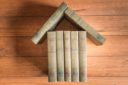 Stack of old books forming the figure of a house on some wooden boards.の写真素材