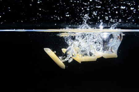 Macaroons falling into the water and splashing drops on black backgroundの写真素材