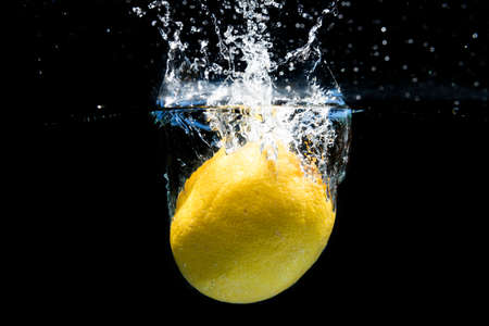 Lemon falling into the water and splashing drops on black backgroundの写真素材