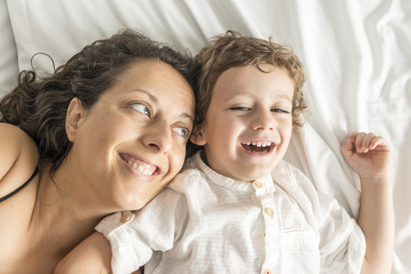 A woman and her son playing in bed and gesturing.の写真素材