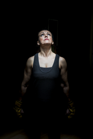Portrait of a woman with boxing gloves on black background and illuminated with overhead light.の写真素材
