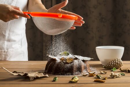Detail of a womanâs hands sprinkling with icing sugar a sponge cake.の写真素材