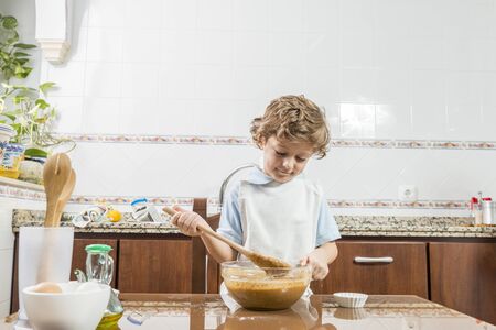 A child cooking a homemade sponge cake, stirring dough from a bowl with a wooden ladle.の写真素材