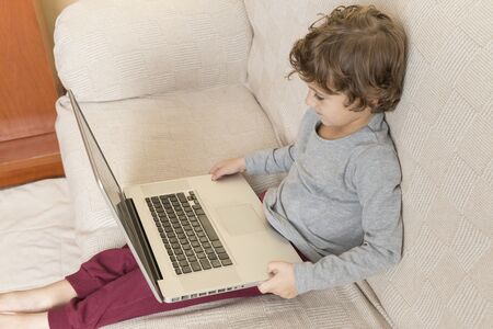 Child sitting on a sofa watching a laptop. Technology concept in childhood.
