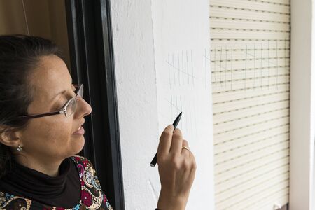 Woman drawing lines on the glass of a window to count the days.の写真素材