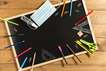 Various school supplies, face mask and hydroalcoholic gel on blackboard. Back to school concept after the pandemic.の写真素材