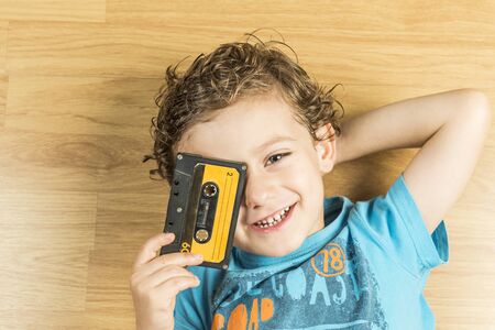 Child looking through the holes of a cassette tape lying on a parquet floor.