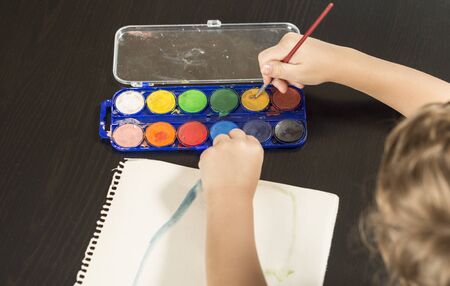 Detail of a child's hands taking a brush and painting with watercolors on paper. Concepts of childhood and back to school.の写真素材