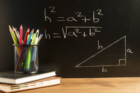 Books, notebooks and a pencil holder with pencils, pens and various school supplies on wooden boards...
