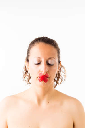 Portrait of a brunette Caucasian woman with closed eyes and mouth covered with X-shaped tape, on white background.の写真素材