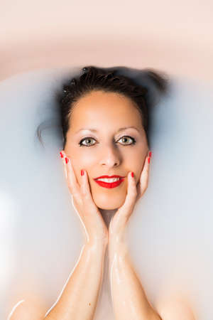 A Caucasian woman taking a bath in a bathtub filled with milk. Body care concept.