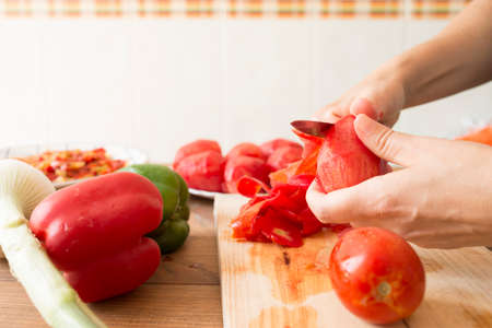 Detail of a woman's hands peeling tomatoes with a knife. Preparation of roasted peppers, a typical dish of Spanish and Andalusian cuisine.の写真素材