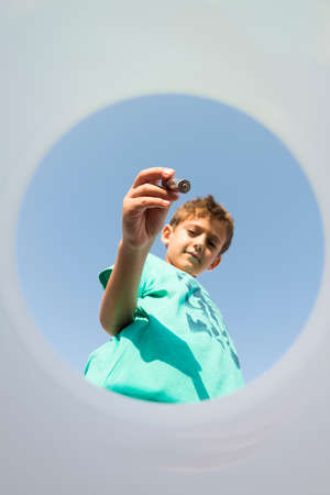 Child placing a pile inside a recycling bin, seen from inside the bin, with a blue sky in the background. Concept of recycling and education in environmental values.の写真素材