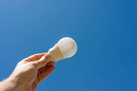 Hand holding an energy saving LED light bulb with a blue sky in the background. Clean energy concept.の写真素材
