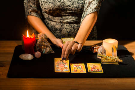 Detail of a woman's hands placing tarot cards on a black card table during a fortune telling session. Concept of a divination session with tarot cards.の写真素材