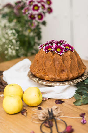 Still life with an apple sponge cake decorated with flowers and kitchen utensils.