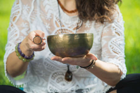 Detail of a woman's hands holding and playing a Tibetan singing bowl during a meditation and music...
