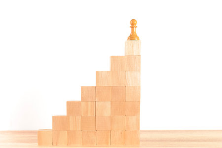 Chess pawn at the top of a staircase made of wooden blocks, with a white background. Concept of self-improvement, leadership and success. Space for copying.の写真素材