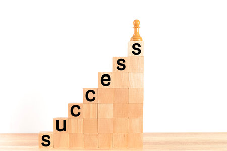 Chess pawn at the top of a wooden block ladder, with the word "success" written on the steps, on a white background. Concept of self-improvement, leadership and success. Space for copying.の写真素材