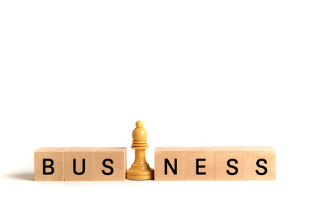 White chess bishop next to wooden blocks forming the word "business", on white background. Image to illustrate the concept of leadership and business strategy.の写真素材