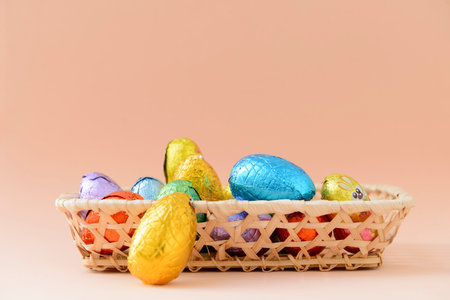 Still life with chocolate Easter eggs in a basket with a background of a soft orange tone.