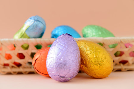 Still life with chocolate Easter eggs in a basket with a background of a soft orange tone.