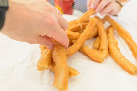 Detail of a man's hand holding a churro. Churros are a traditional breakfast in Spain.の写真素材