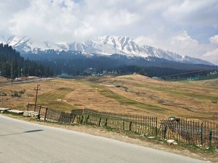 A landscape shot of mountain range of kashmir valley with dry field as foreground along the road