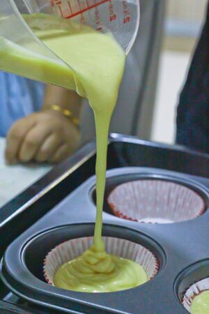A shot of flour mixture being carefully poured into cupcake traysの写真素材