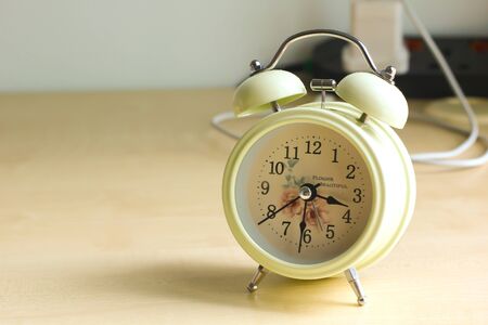 A close up shot of a beige color alarm clock on a wooden tableの写真素材
