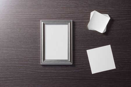 Empty, beautiful, photo frame and empty white paper cards for notes on the background of a table made of dark, textured wood. Empty space. Stylized stock photos. The view from the top.の写真素材