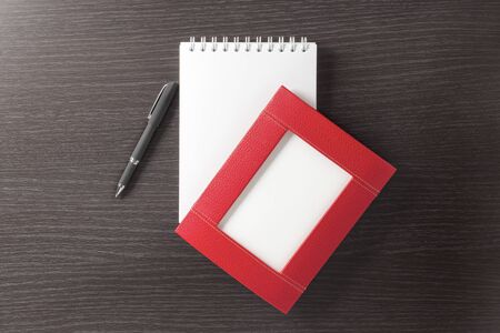 An empty, beautiful, red leather photo frame, an empty spiral notebook, and a stylish corporate pen...