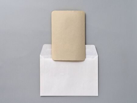 An empty Kraft brown card for an invitation or greeting and a white paper envelope on a gray...