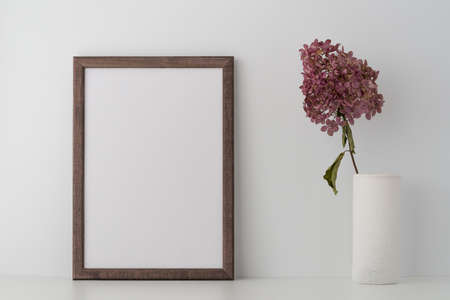 An empty wooden frame and dry decorative branch in a vase on a shelf or table, near a white wall. Whites colors. Clean, modern, minimal frame, the layout of the poster. Internal interior.の写真素材