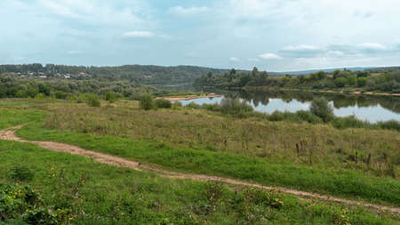 View of the winding river on a summer day. In the foreground is a winding country road and a green...