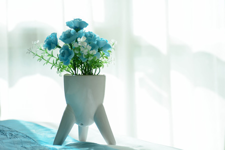 white vase with blue plastic flower on the bedの写真素材