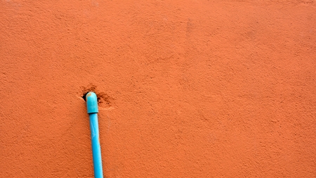 blue plastic pipe at orange cement wall.