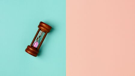 old hourglass on blue and pink background