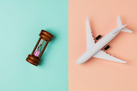 Model airplane and hourglass on blue and pink background.