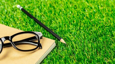 pencil, diary book and a glasses on green grass lawn in the morning.の写真素材