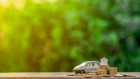 Grey miniature car model and small house on pile coins. - Finance and car loan, saving money for a car concepts.の写真素材