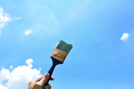 Hand holding the paintbrush on blue sky background