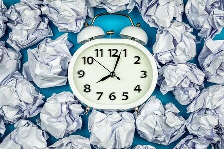 white alarm clock with pile of a crumpled paper balls. - thinking and timing ideas concept.