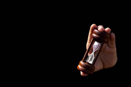hand holding a classic wood hourglass isolated on black background.