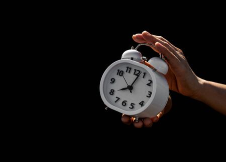 Hand holding a white alarm clock in the dark. - thinking and control timing ideas concept.の写真素材