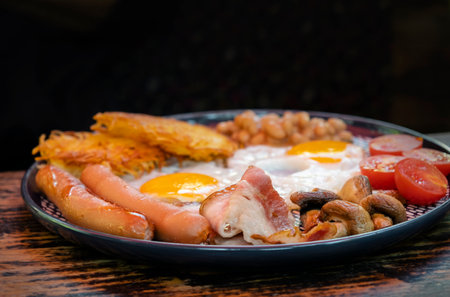 Traditional English Breakfast. Fried eggs, sausages, beans, mushrooms and bacon on plate on the wooden table. High quality photoの写真素材