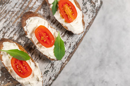 Cream cheese sandwiches with tomato and greens on grey wooden board, appetizer easy recipe, space for text. High quality photoの写真素材
