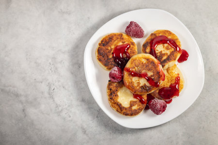 Curd fritters with raspberry and syrup in white plate on the light grey background, selective focus. High quality photoの写真素材